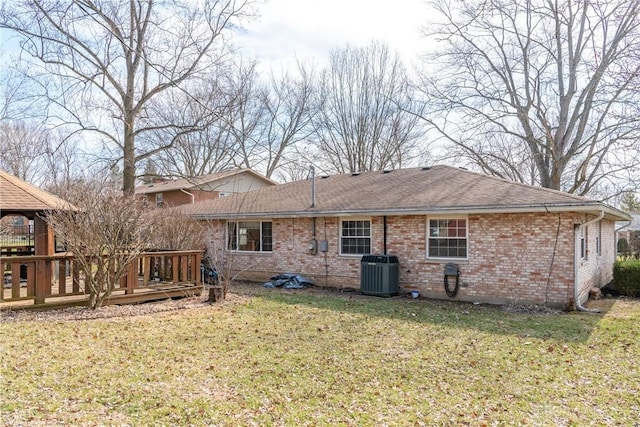 rear view of house with central AC unit, brick siding, roof with shingles, a lawn, and a wooden deck