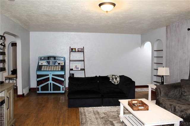 living room featuring arched walkways, built in shelves, a textured ceiling, and dark wood finished floors