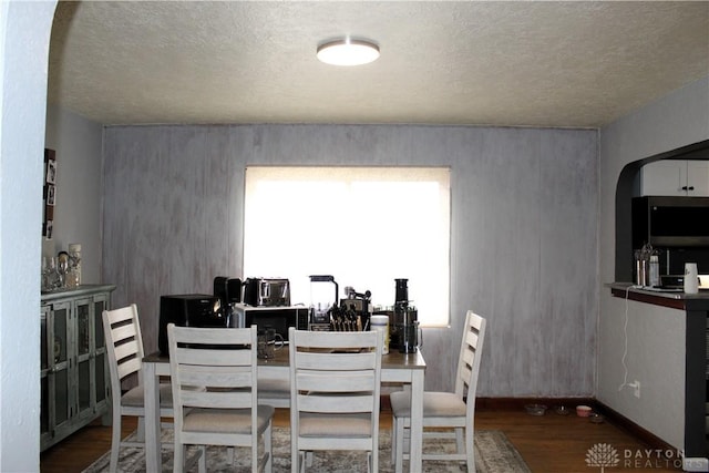 dining area with baseboards, arched walkways, and wood finished floors