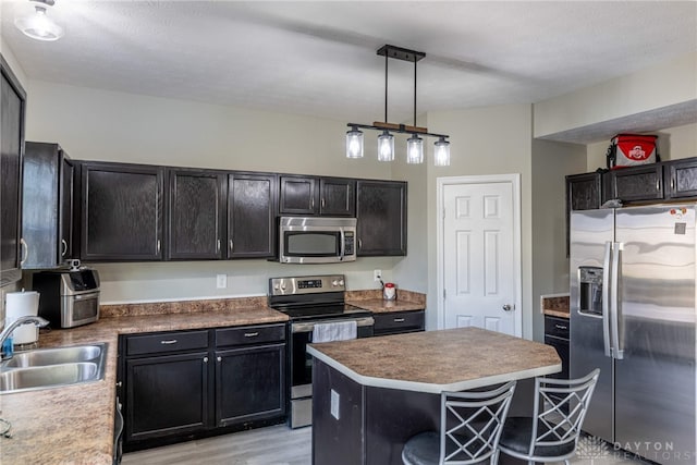 kitchen with light wood finished floors, appliances with stainless steel finishes, a sink, a kitchen island, and dark cabinets