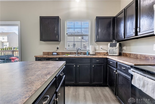 kitchen featuring range with electric stovetop, a sink, light wood-style flooring, and dark cabinets