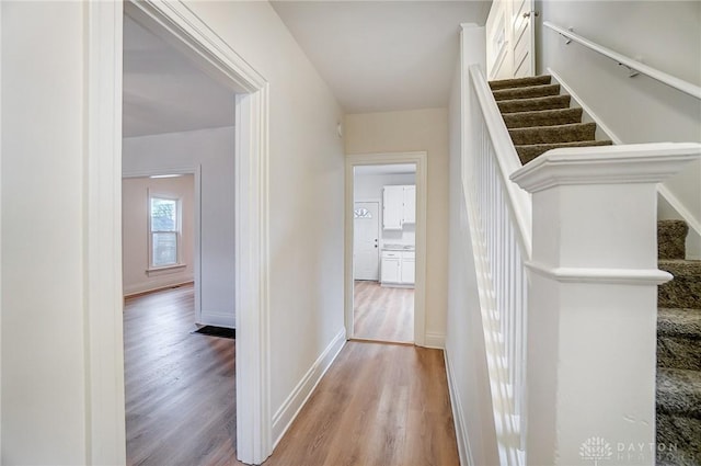 corridor featuring stairs, baseboards, and light wood-style floors