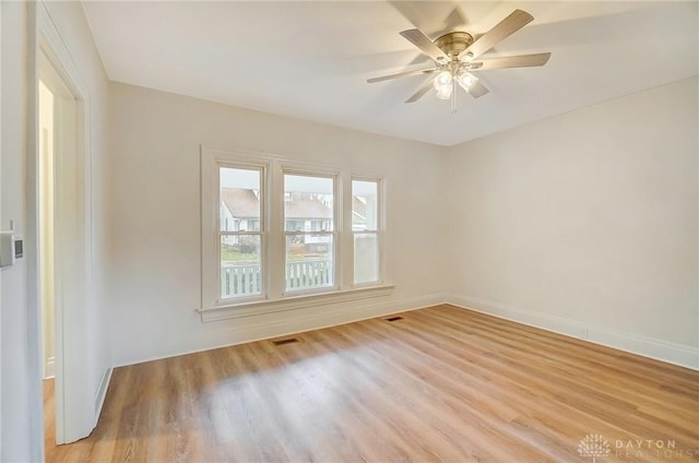 empty room featuring a ceiling fan, light wood-style flooring, visible vents, and baseboards