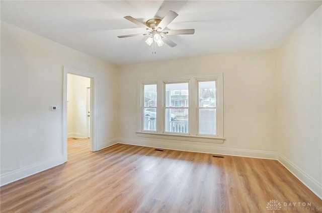 empty room featuring a ceiling fan, visible vents, light wood-style flooring, and baseboards