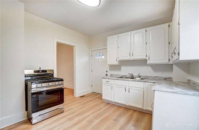 kitchen featuring a sink, light wood-style floors, baseboards, white cabinets, and stainless steel gas stove