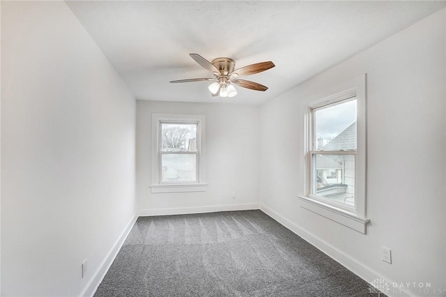 spare room featuring a ceiling fan, dark colored carpet, and baseboards