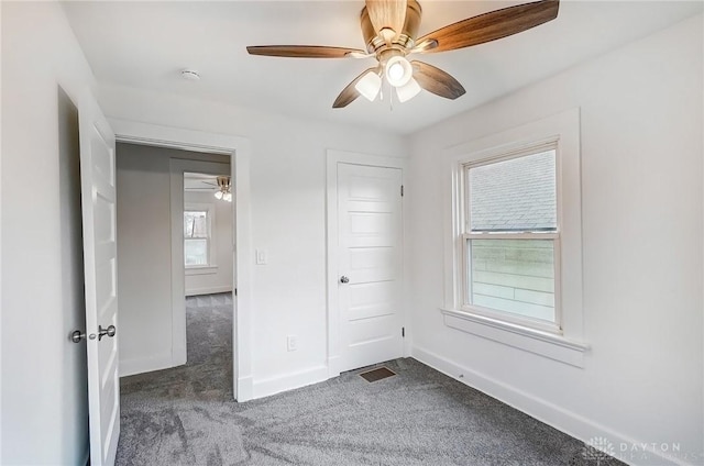 unfurnished room featuring baseboards, visible vents, dark colored carpet, and a ceiling fan