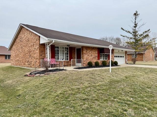 single story home with driveway, brick siding, an attached garage, covered porch, and a front yard