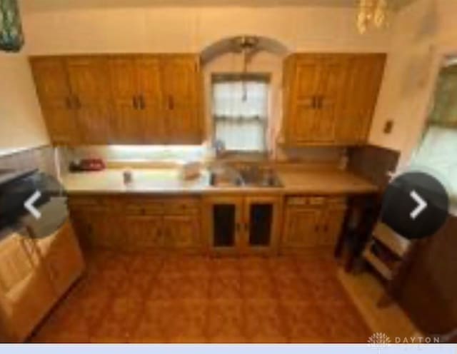 kitchen with glass insert cabinets, brown cabinets, a sink, and light countertops