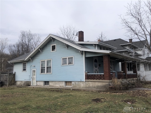 back of property with covered porch, a lawn, and a chimney