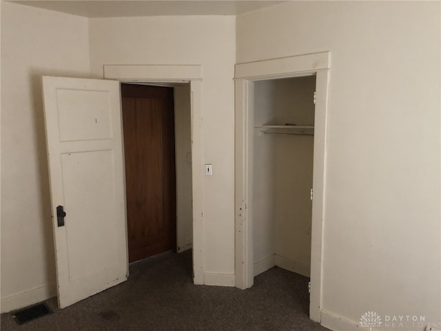 unfurnished bedroom featuring dark colored carpet, a closet, visible vents, and baseboards