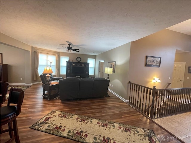 living room with ceiling fan, a textured ceiling, baseboards, and wood finished floors