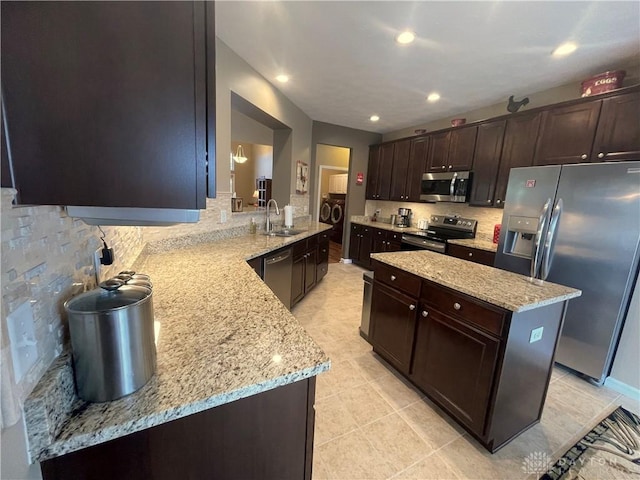 kitchen with backsplash, appliances with stainless steel finishes, a sink, dark brown cabinets, and light stone countertops