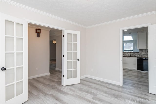 empty room featuring light wood-type flooring, baseboards, french doors, and ornamental molding