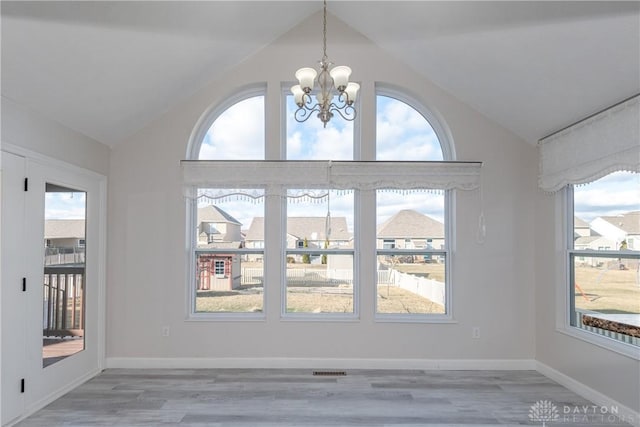 interior space with light wood-style floors, a notable chandelier, vaulted ceiling, and baseboards