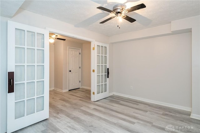 empty room with french doors, a textured ceiling, baseboards, and wood finished floors