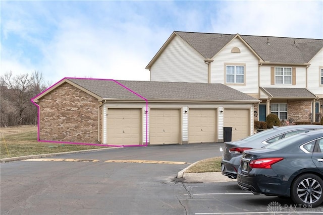 view of property with driveway, brick siding, an attached garage, and a shingled roof