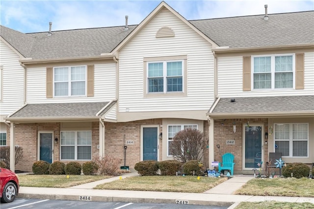 multi unit property featuring a shingled roof, uncovered parking, and brick siding