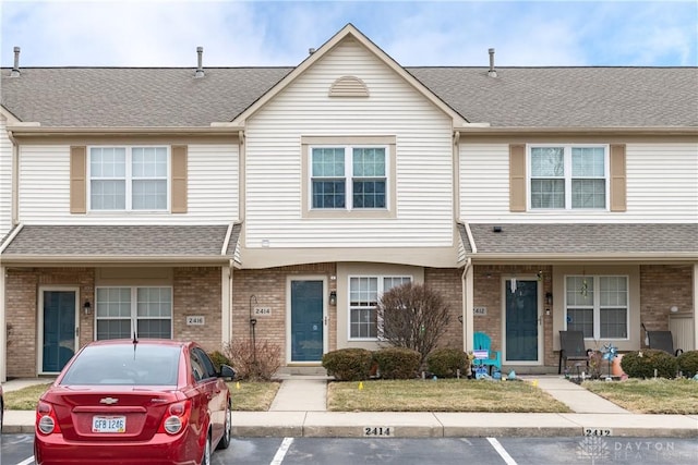 townhome / multi-family property with a shingled roof, uncovered parking, and brick siding