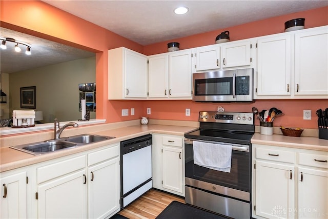 kitchen featuring appliances with stainless steel finishes, white cabinets, a sink, and light wood finished floors