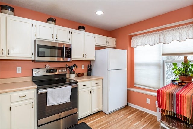 kitchen with appliances with stainless steel finishes, light countertops, light wood finished floors, and white cabinetry