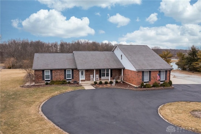 view of front of property featuring aphalt driveway, a front yard, brick siding, and a porch