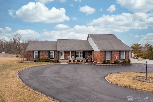 view of front facade featuring a front yard, brick siding, and curved driveway