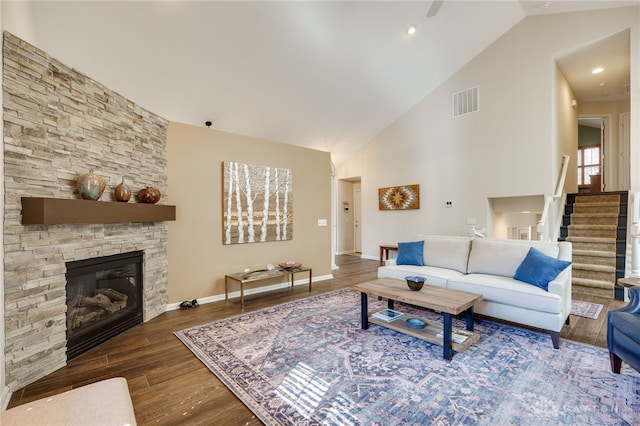 living room featuring high vaulted ceiling, a fireplace, wood finished floors, visible vents, and stairs