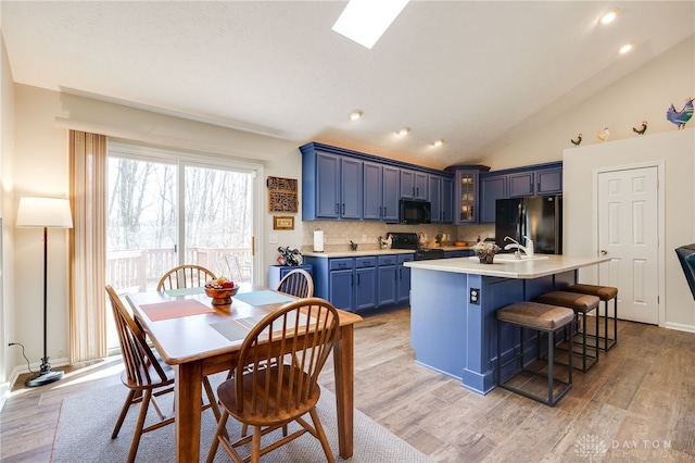 kitchen with lofted ceiling with skylight, glass insert cabinets, blue cabinetry, light countertops, and black appliances