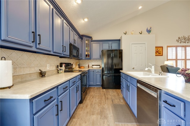 kitchen featuring lofted ceiling, glass insert cabinets, blue cabinetry, black appliances, and a sink