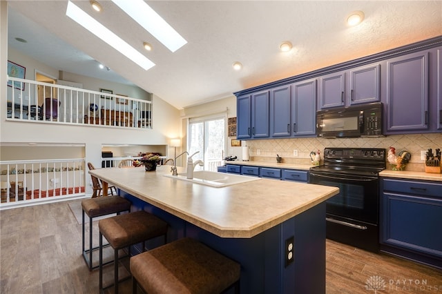 kitchen with blue cabinets, black appliances, a kitchen bar, and wood finished floors