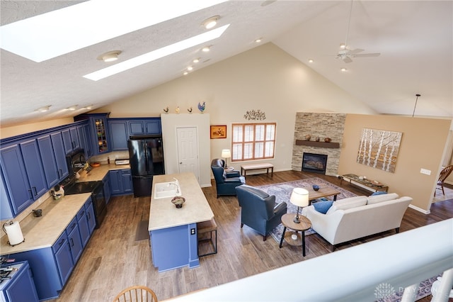 living area with high vaulted ceiling, a stone fireplace, a skylight, and light wood-style floors