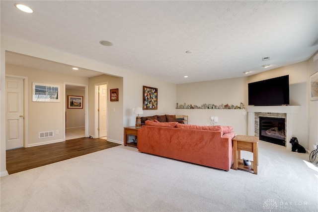 carpeted living area featuring a textured ceiling, a fireplace with flush hearth, visible vents, and recessed lighting