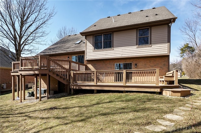 back of property with a deck, roof with shingles, brick siding, and a lawn