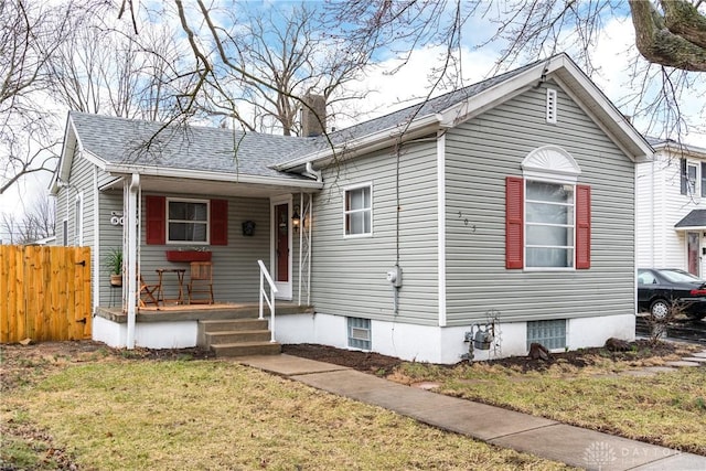 view of front of house featuring a shingled roof, covered porch, fence, and a front lawn