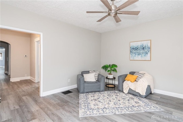 sitting room with visible vents, a textured ceiling, arched walkways, and wood finished floors