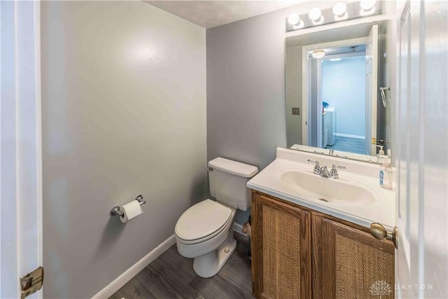 half bath with toilet, baseboards, wood finished floors, and vanity