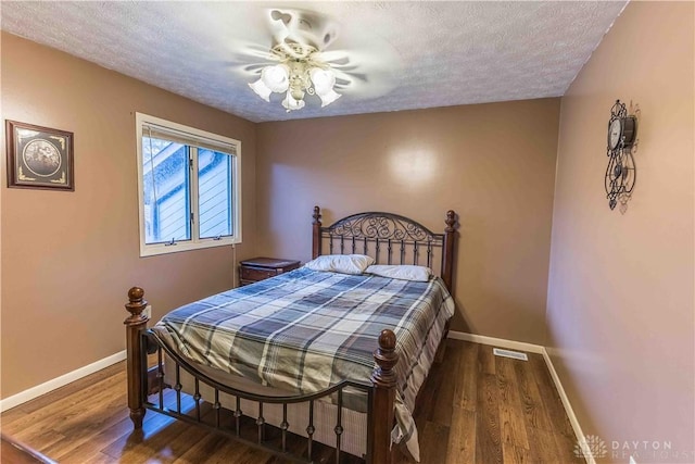 bedroom featuring a textured ceiling, baseboards, and wood finished floors