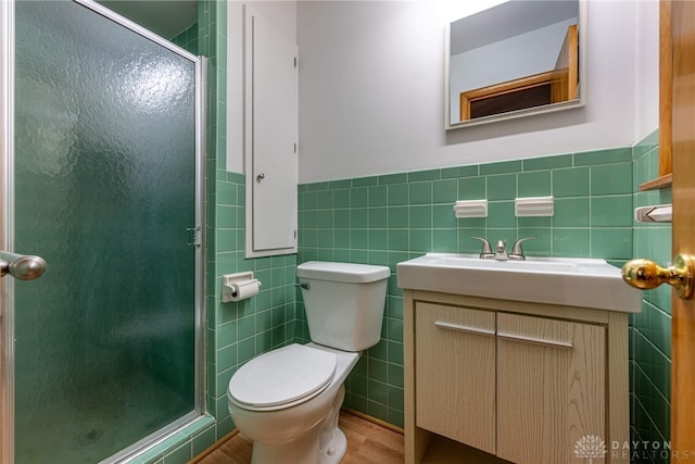 bathroom with toilet, a wainscoted wall, vanity, tile walls, and a stall shower