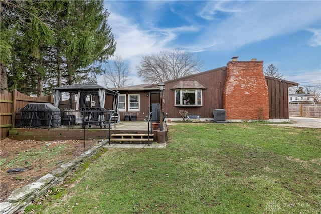 rear view of property with central air condition unit, fence, a gazebo, a yard, and a chimney