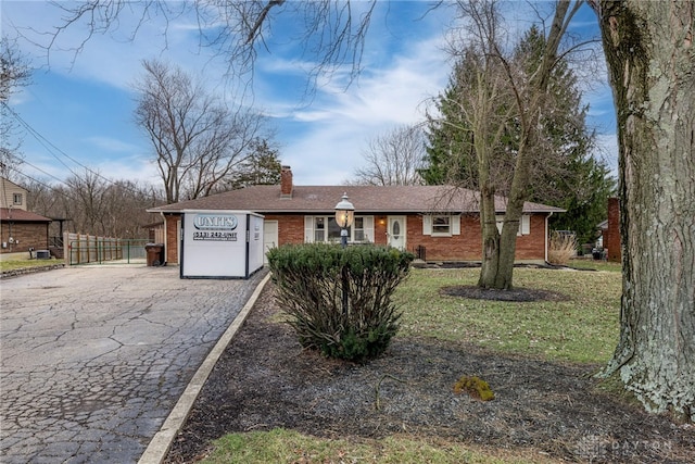 single story home featuring aphalt driveway, a front yard, brick siding, and a chimney