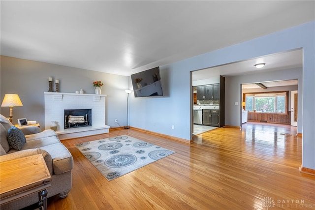 living room featuring light wood-style floors, a brick fireplace, and baseboards