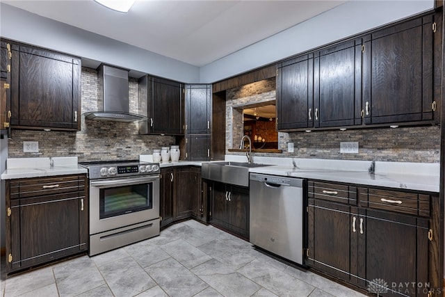 kitchen featuring a sink, appliances with stainless steel finishes, backsplash, and wall chimney range hood