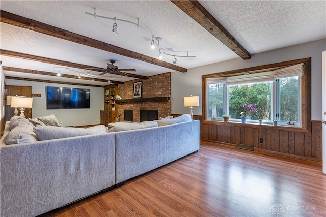 living area featuring a wainscoted wall, a fireplace, a textured ceiling, wood finished floors, and beamed ceiling