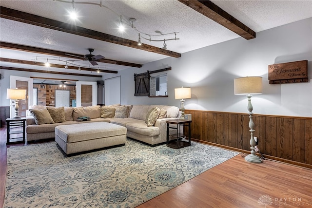 living room with a wainscoted wall, beamed ceiling, a textured ceiling, and a barn door