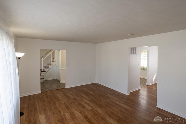 unfurnished room with stairs, visible vents, baseboards, and wood finished floors