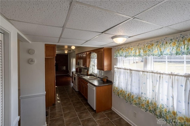 kitchen featuring brown cabinets, dark countertops, dark tile patterned flooring, white appliances, and a drop ceiling