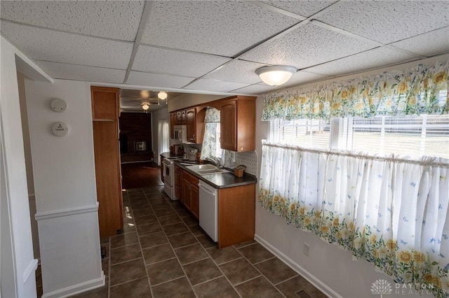 kitchen featuring dark countertops, a paneled ceiling, a sink, dark tile patterned flooring, and white appliances