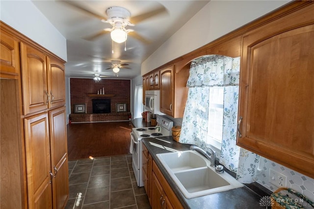 kitchen with brown cabinets, a fireplace, a sink, dark tile patterned flooring, and white appliances