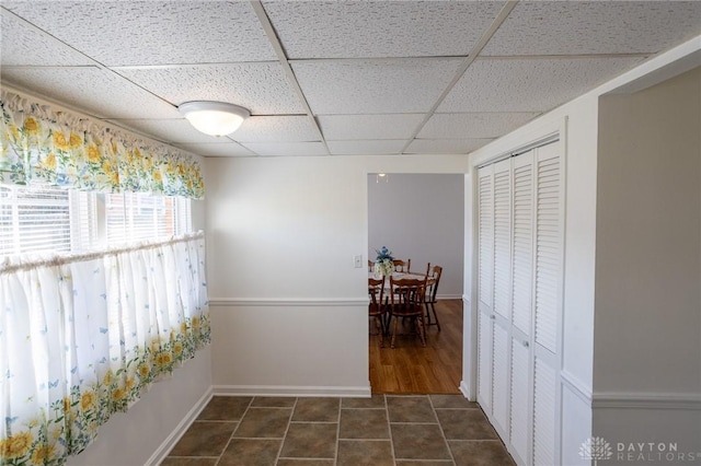 hall with dark tile patterned floors, a paneled ceiling, and baseboards